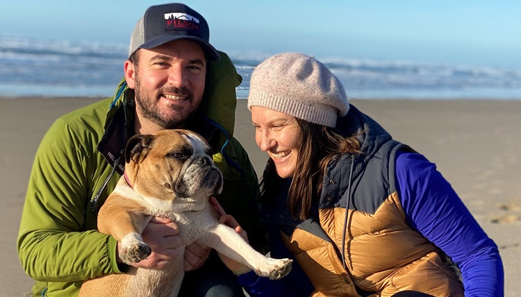 Phil Brytzwa poses with his dog and a woman on the beach.