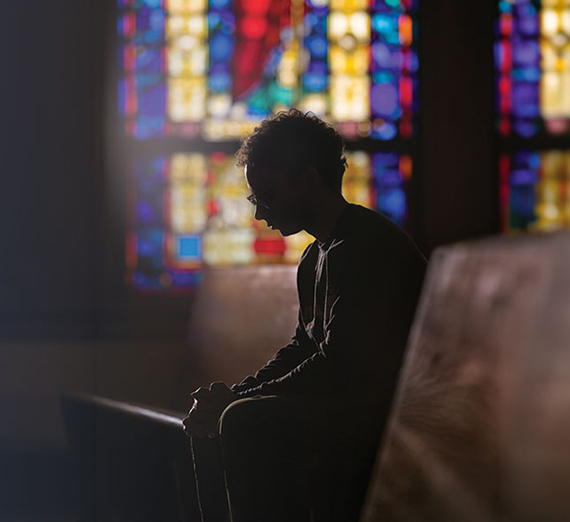 student in chapel with stained glass windows