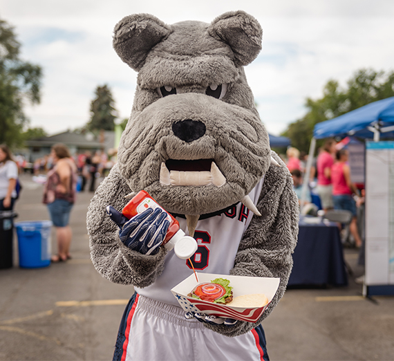 Spike the mascot, is excitedly putting ketchup on a burger. 