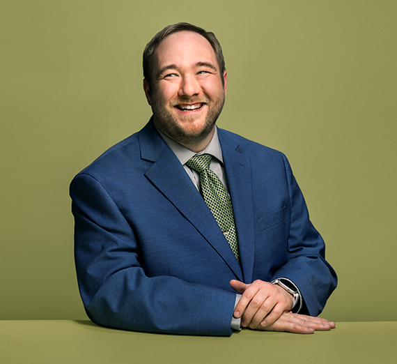 Neil Christenson (’25 J.D.) smiling in a blue suit and green tie.