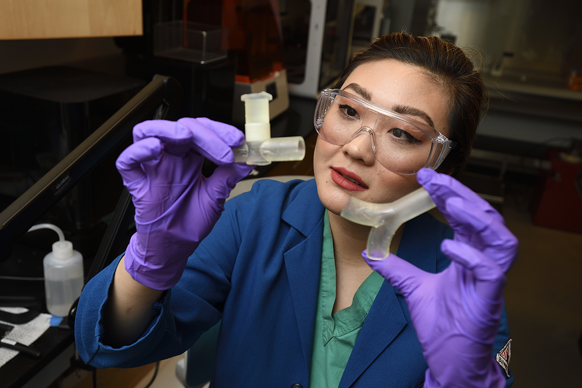 Helen Xun shows off two forms of ventilator splitters she is helping to design and 3D print. (Photo: Will Kirk / Johns Hopkins University)