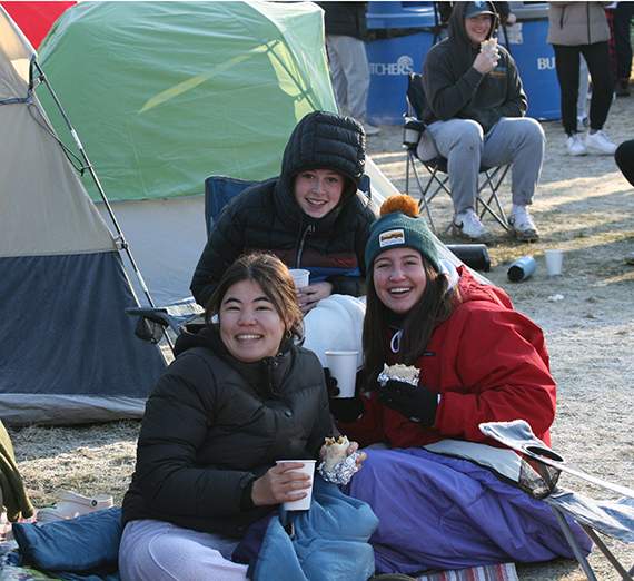 Three students huddled in blankets outside a tent at Kennel Campout