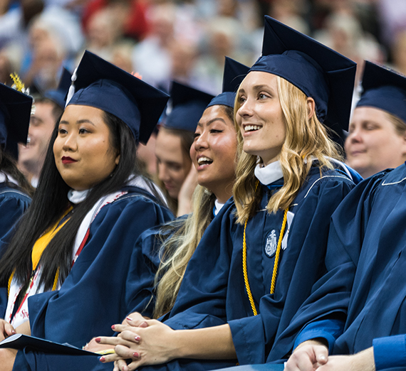 graduates in gowns listen during ceremony