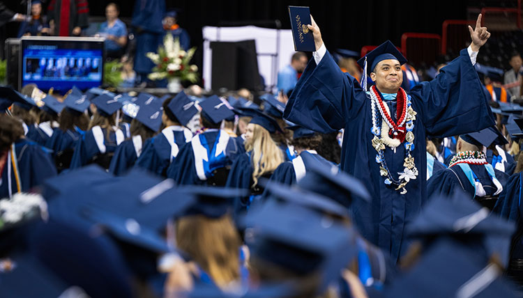 A graduate raises his arms with joy after receiving his degree