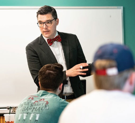 Andrew Brajcich standing in front of a white board while students look at him