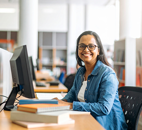 A woman sitting with books and computer looks at the camera in image generated by AI