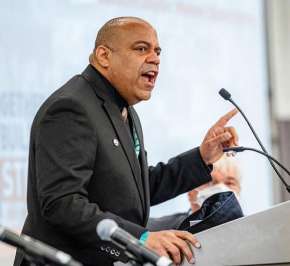 Eric Ward speaks into a microphone at a podium