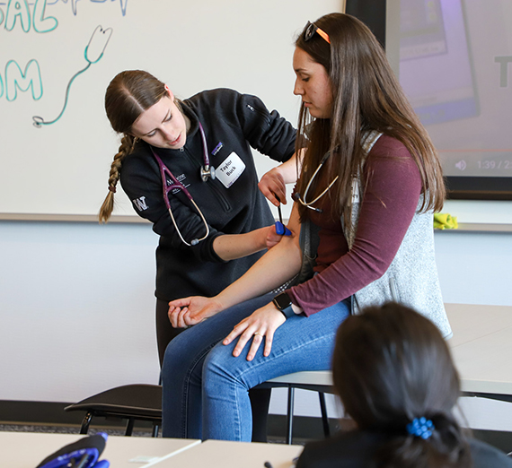 A teacher takes the blood pressure of a woman