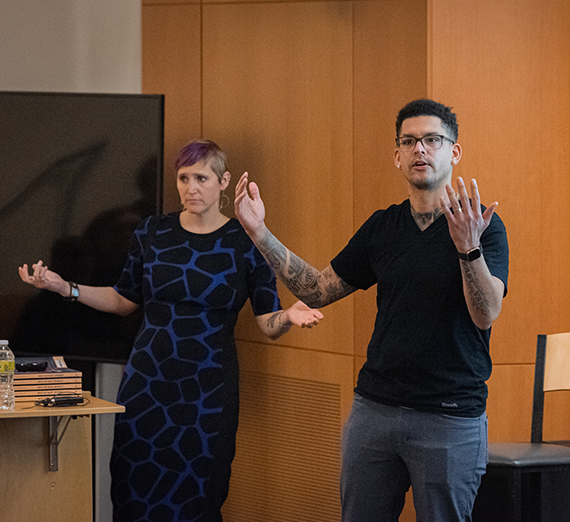 Philosophers Jennifer Kling and Leland Harper standing with arms extended in Hemmingson Auditorium. 