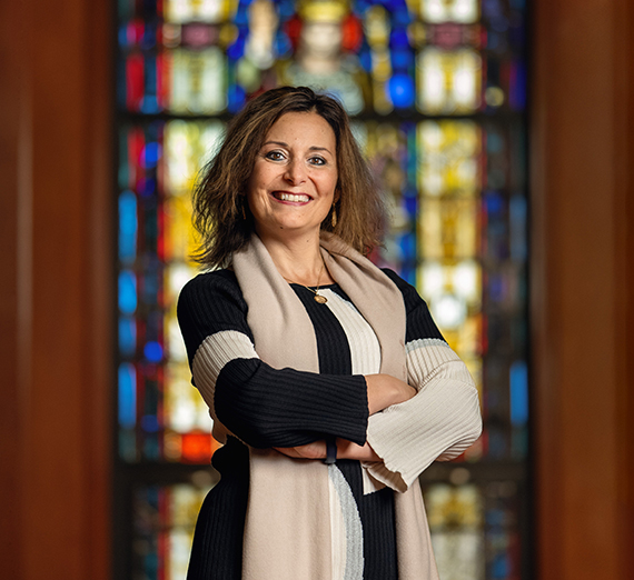 Gonzaga President Katia Passerini standing in front of a stained glass window with her arms crossed