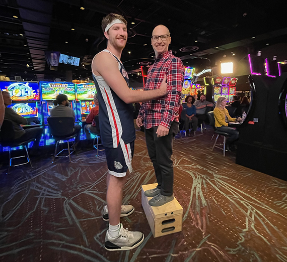 Drew Timme stands next to actor Mark Robbins, who is standing on a crate to equal Timme's height