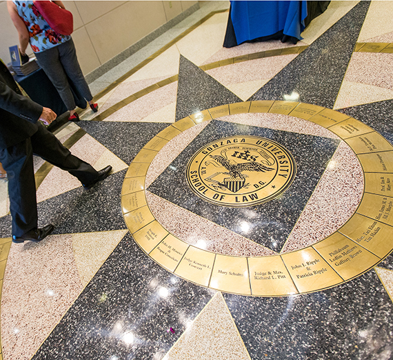 People walking past the law school logo embedded in the floor