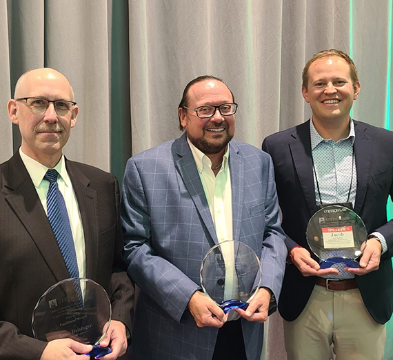 Law school Dean Jacob Rooksby stands to the right holding an award plaque, joined by two other men