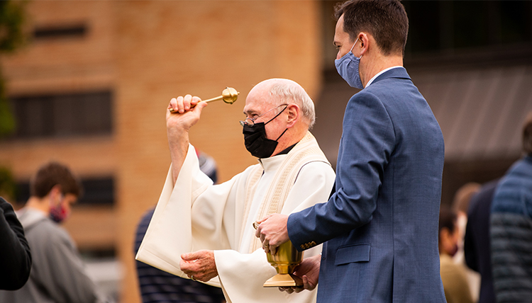 Jesuit priest blessings attendees at commencement Mass