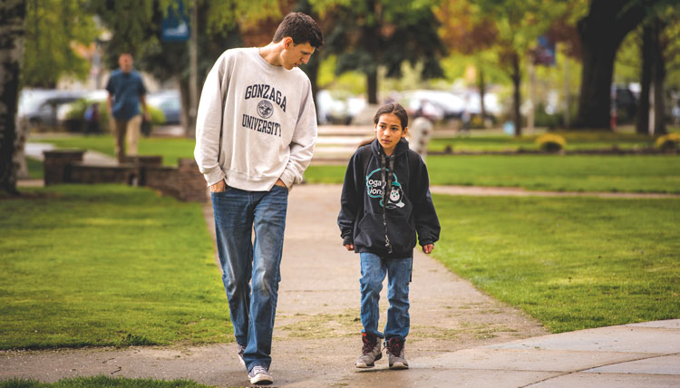 male college student walks outdoors with middle school student