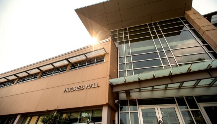 A shot of the front of Hughes Hall, taken looking upward. The sun is peeking out behind the bulding.