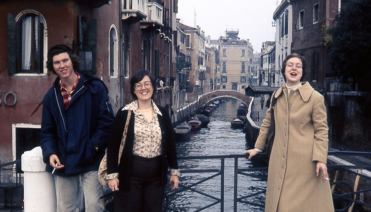 A group of three students smiling together on a bridge in Venice, Italy.