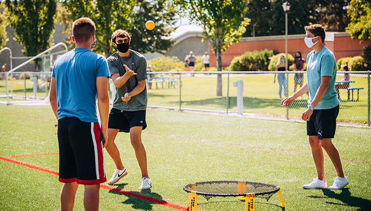 A group of students play spike ball while wearing masks on Mulligan Field.