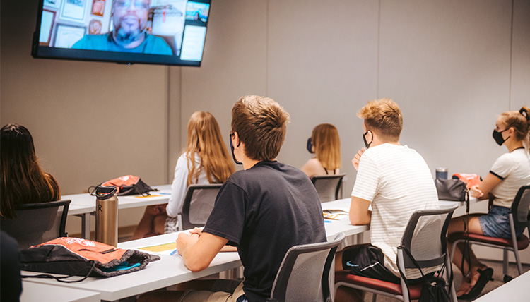 A group of students watches a speaker on Zoom in a classroom.