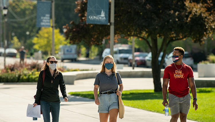 Three people walk through campus with masks. 