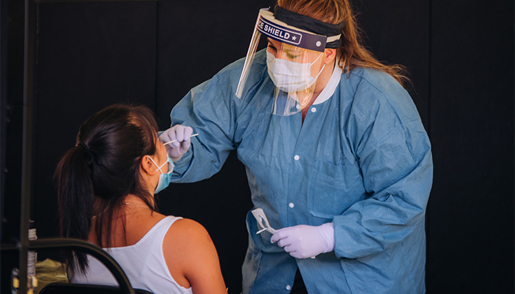 A student is tested for covid-19 by a nurse wearing personal protective equipment.