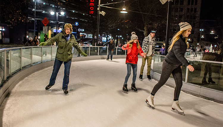 Three people ice skate around a corner on the ice ribbon.