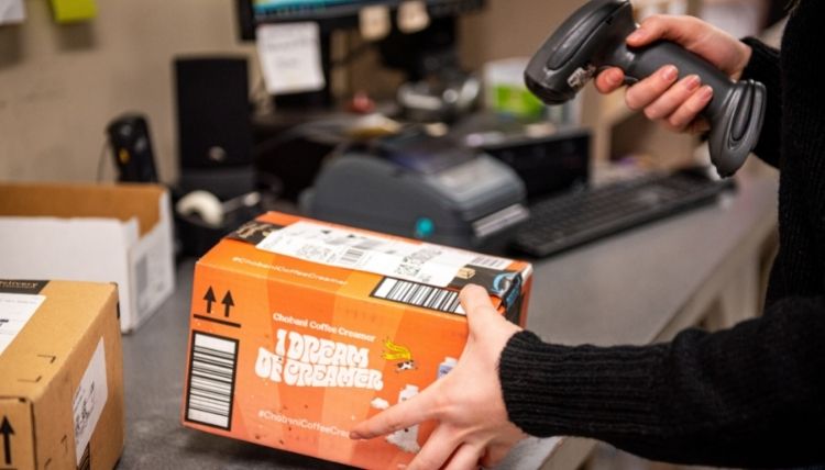 Photo of Mail Services worker scanning an orange, medium-sized box. Only the hands and box can be seen. 