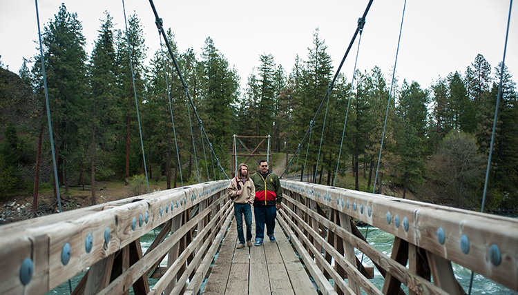 Two students walk across a hanging wooden bridge at Riverside State Park.