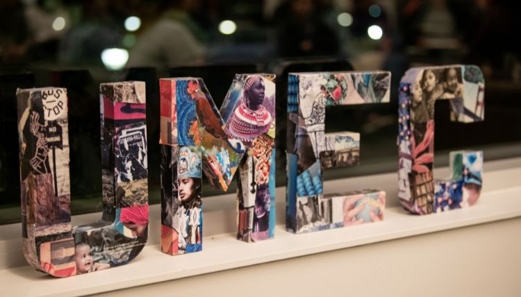 The letters 'UMEC' on a window sill. The letters are made up of photos from various cultural and racial identities and from social justice art. The scene behind the window is dark; the photo was assumedly taken at night.