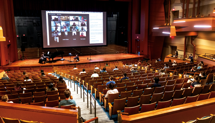 students seated far apart in Woldson Theatre with performance on screen