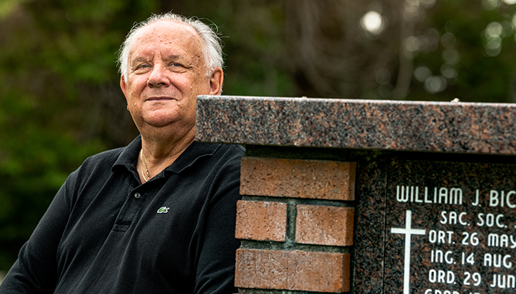 man leans against crypt at Jesuit cemetery in Spokane