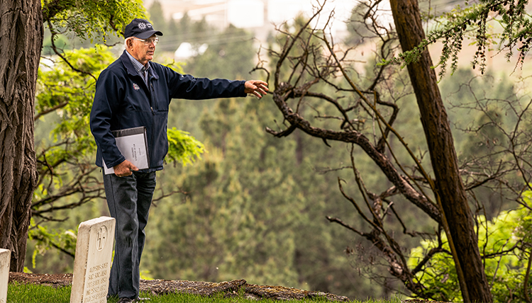 man stands at edge of Jesuit cemetery on hilltop in Spokane