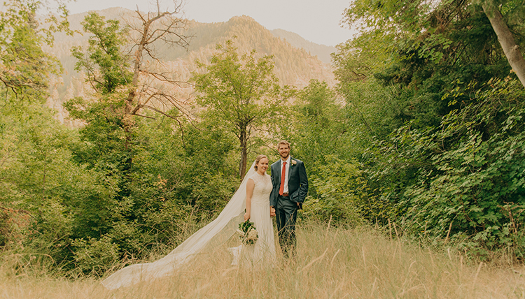 Man and women pose in a field with a long veil. 