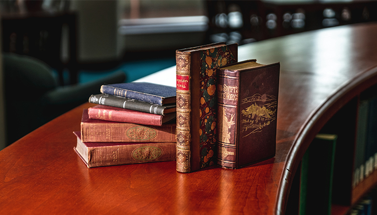 Rare books, covers slightly worn, standing and piled together on a table in Foley Library.