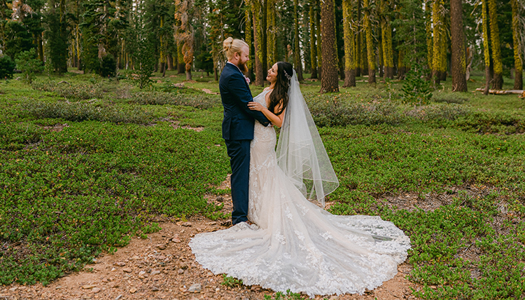 Man and woman pose in wedding outfits in forest.