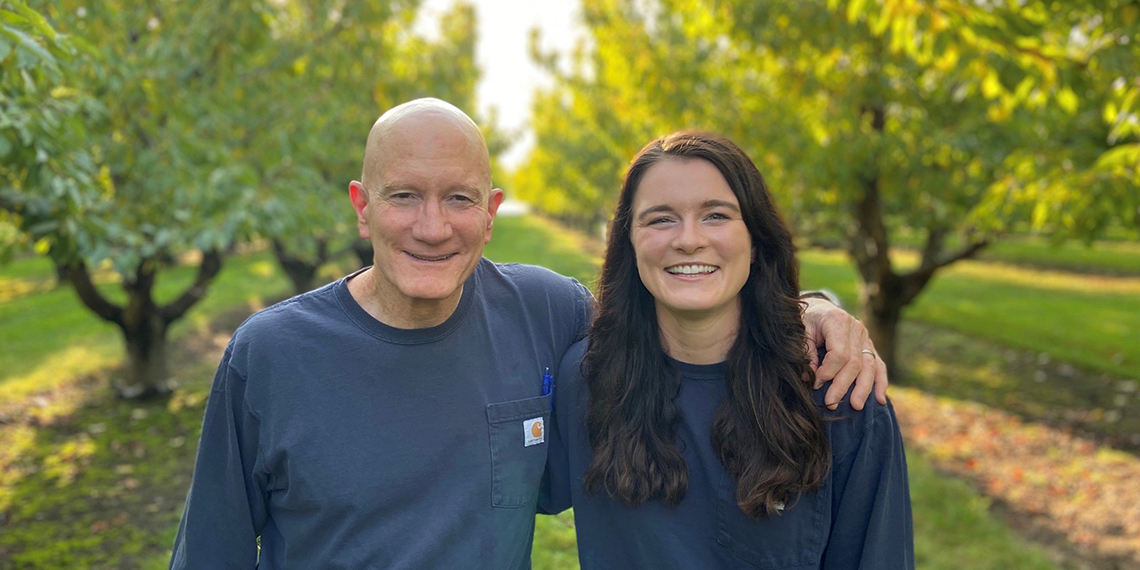 Bart and Bridget stand on Horrigan Farms in front of some trees.