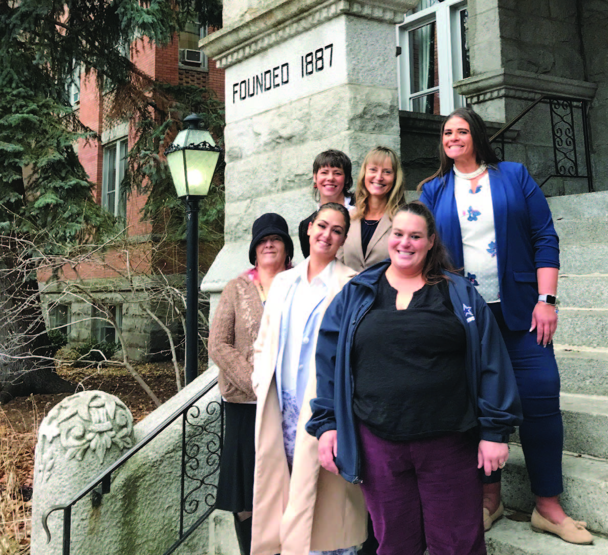 The group of smiling essential skills participants stand on the steps of College hall. 