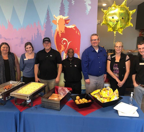 7 Sodexo employees standing behind a food table posing for a picture. 