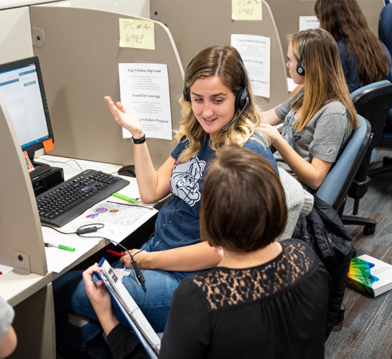 A student telefund employee speaks with her supervisor while working on the computer during her shift.