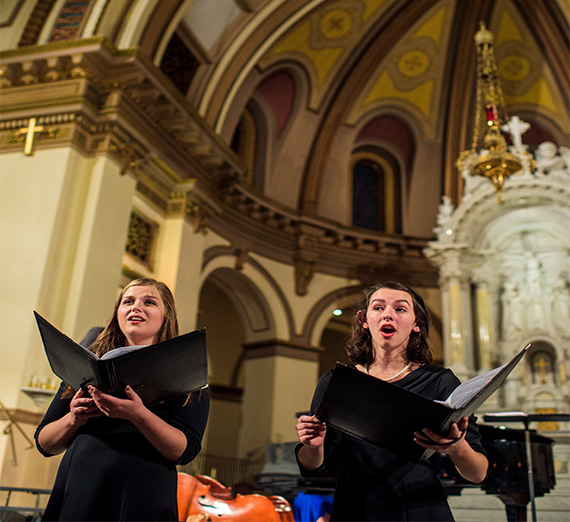 Two girls sing from their choir books in the church.