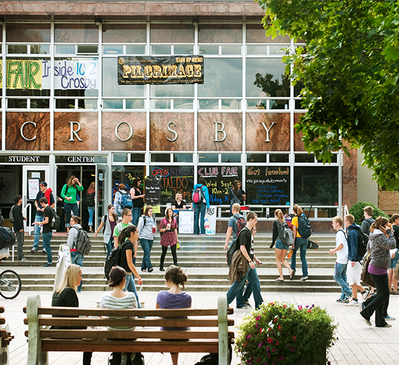 Students walk through campus with signs nearby advertising for a club fair.