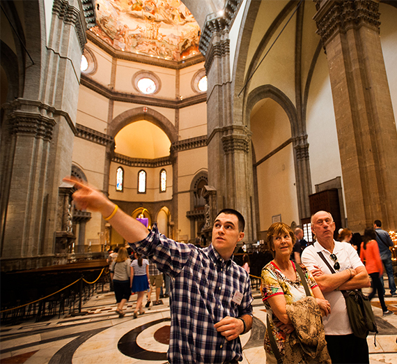 A student tour guide points to and explains something in a cathedral in Florence, Italy.