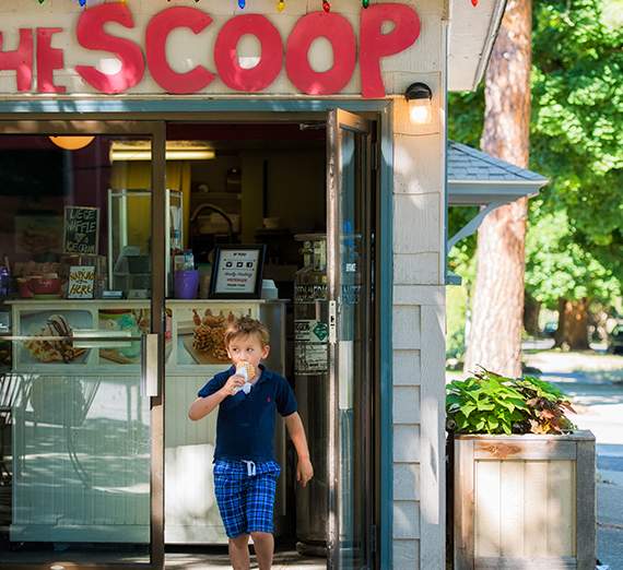 A young boy walks out of an ice cream shop licking an ice cream cone. 