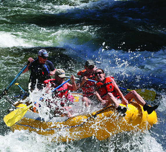 A group of students are hit with a wave as a guide navigates their raft through whitewater.