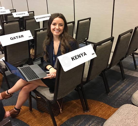 A student participating in Model UN sits next to a sign that says Kenya.