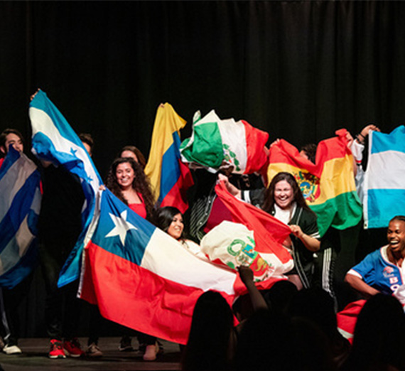 A group of students from La Raza holds up flags from Spanish-speaking countries.  