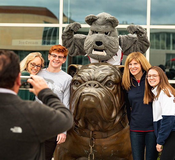 A man takes a photo of his family with a bulldog statue and Spike the bulldog mascot.