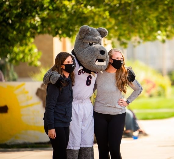 Two masked students posing with Spike the Bulldog outside during orientation weekend 