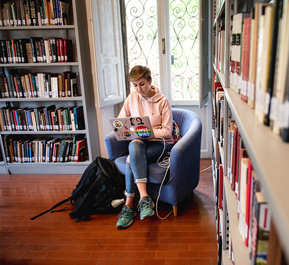 A student works on her computer sitting in a chair in the library. 