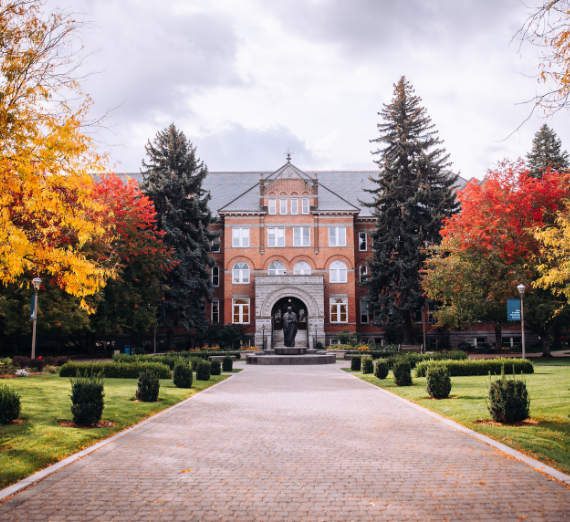 A front-facing shot of College Hall in fall, surrounded by red, yellow, and green trees. 